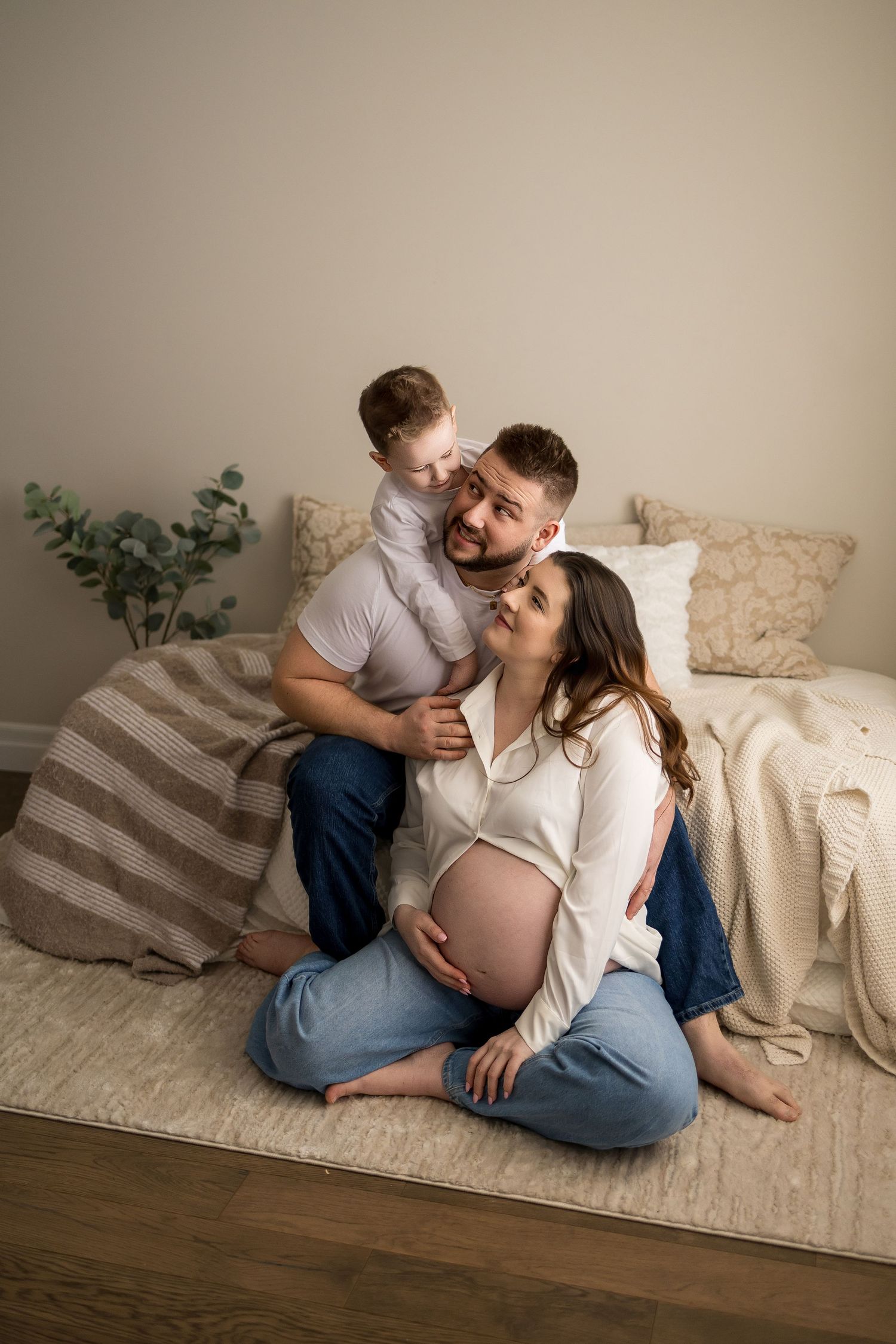 A loving family moment captured on a couch with an expectant mother in a white sweater and jeans.