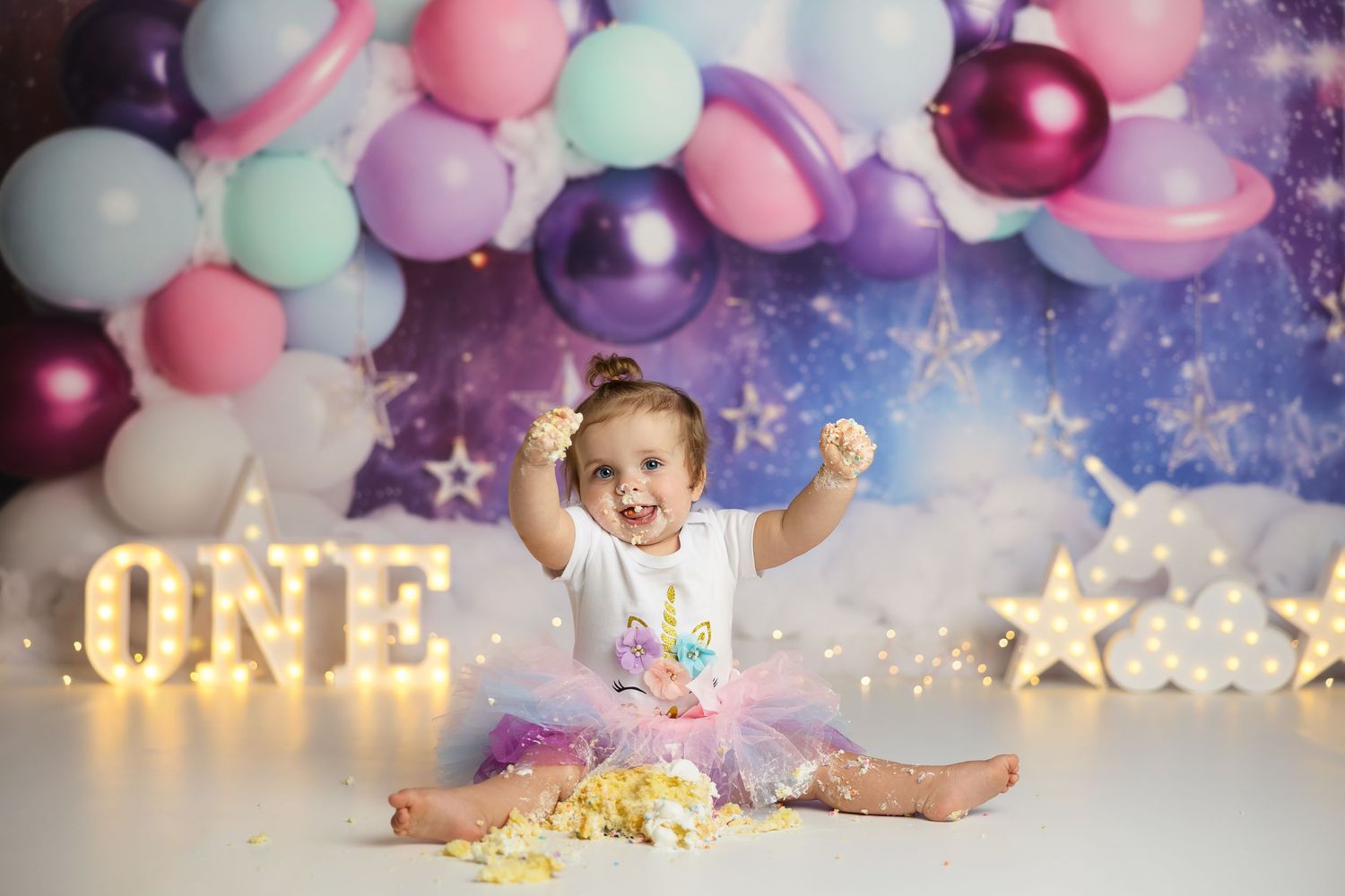 Purple and pink balloon decorated cake smash setup with sparkly accents.