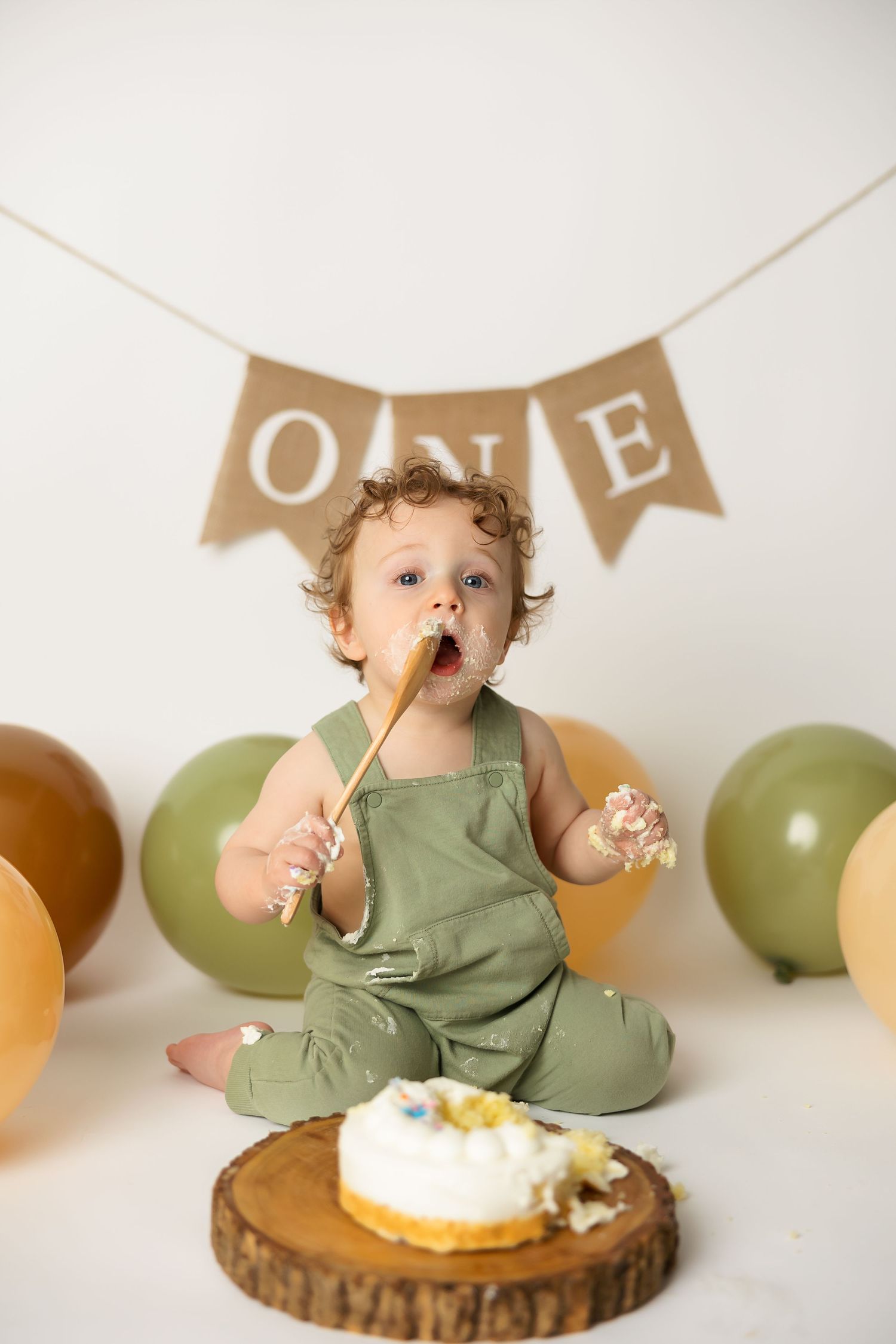 One year old in green romper tasting cake during first birthday photoshoot.