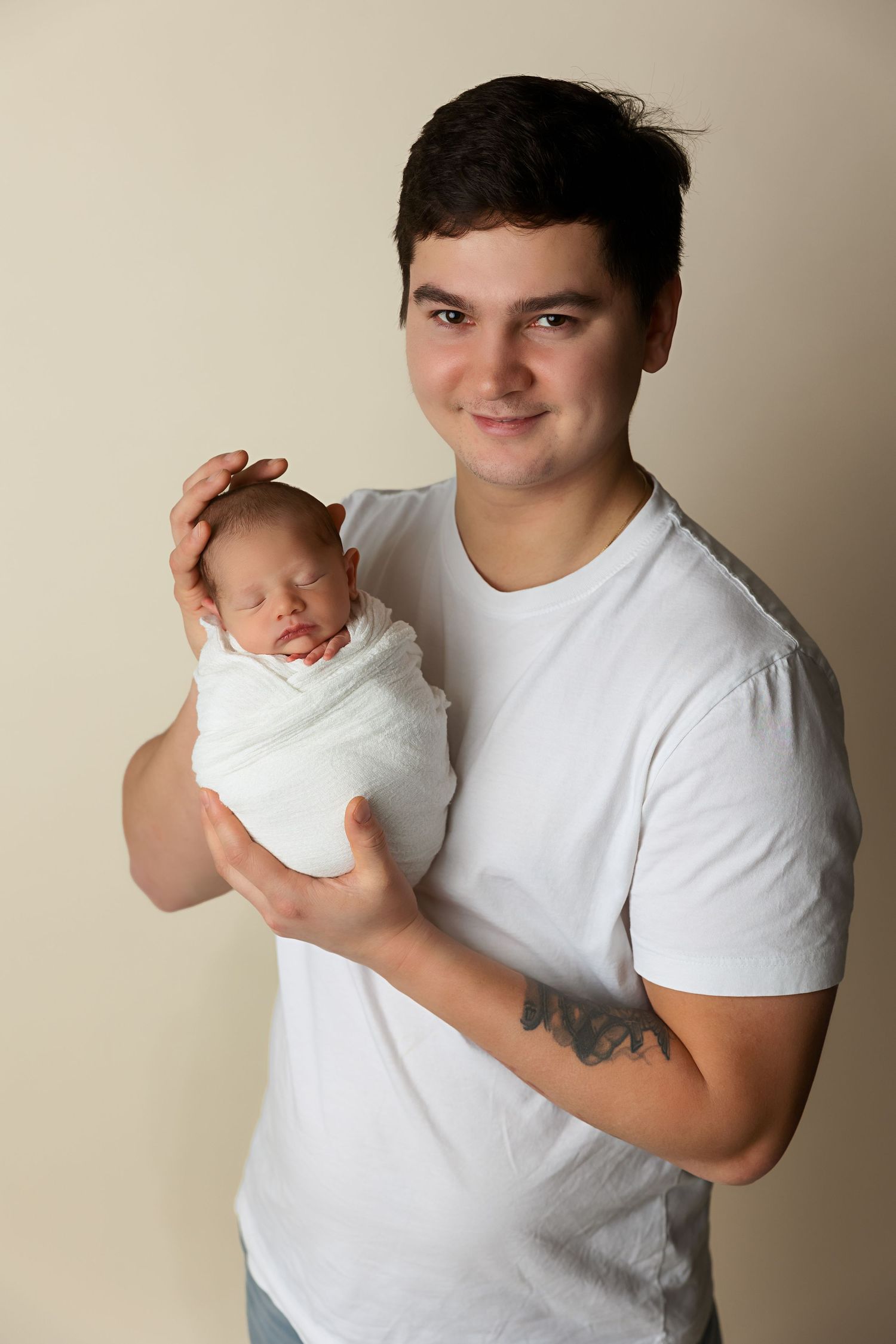 Parent in white shirt gently holds swaddled newborn baby while smiling at camera.