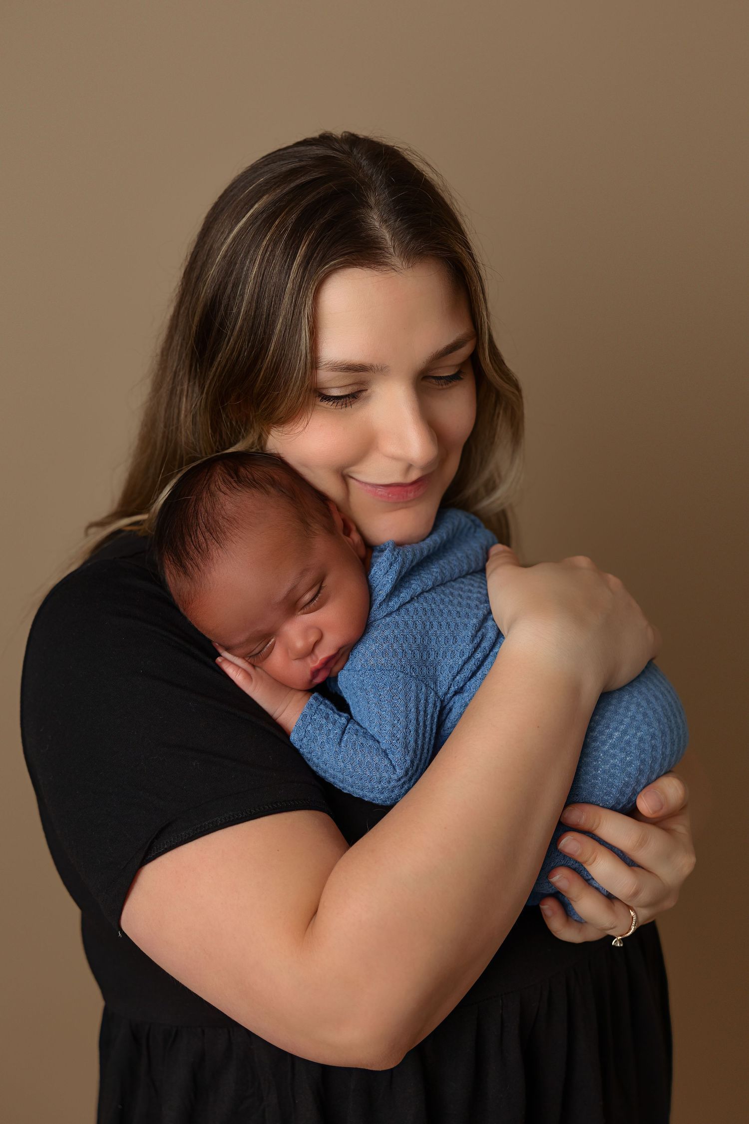 Tender moment between parent and sleeping baby wrapped in blue against neutral background.