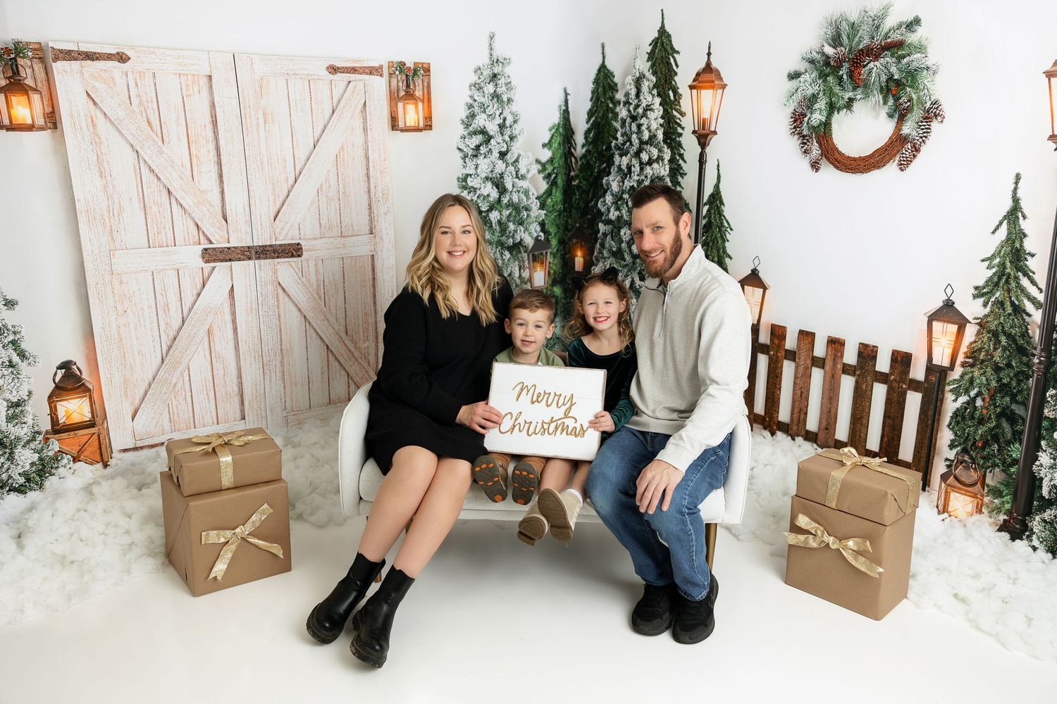 Family poses together on white couch with Christmas decorations and wrapped presents.