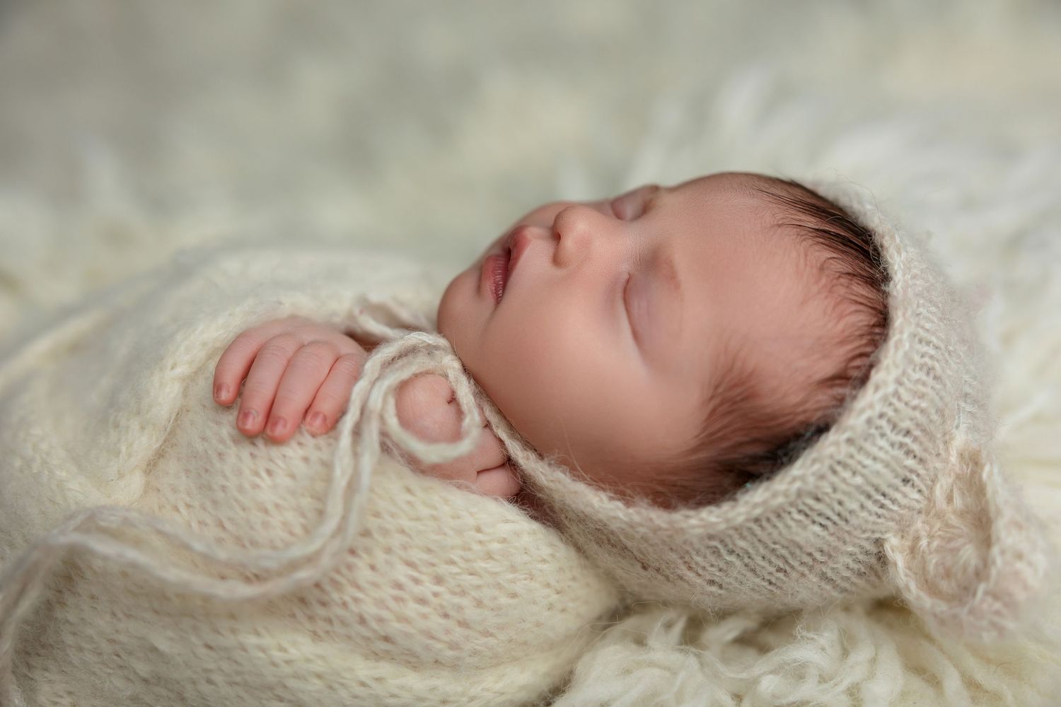 Close-up of sleeping newborn wrapped in soft cream knit blanket showing peaceful expression.