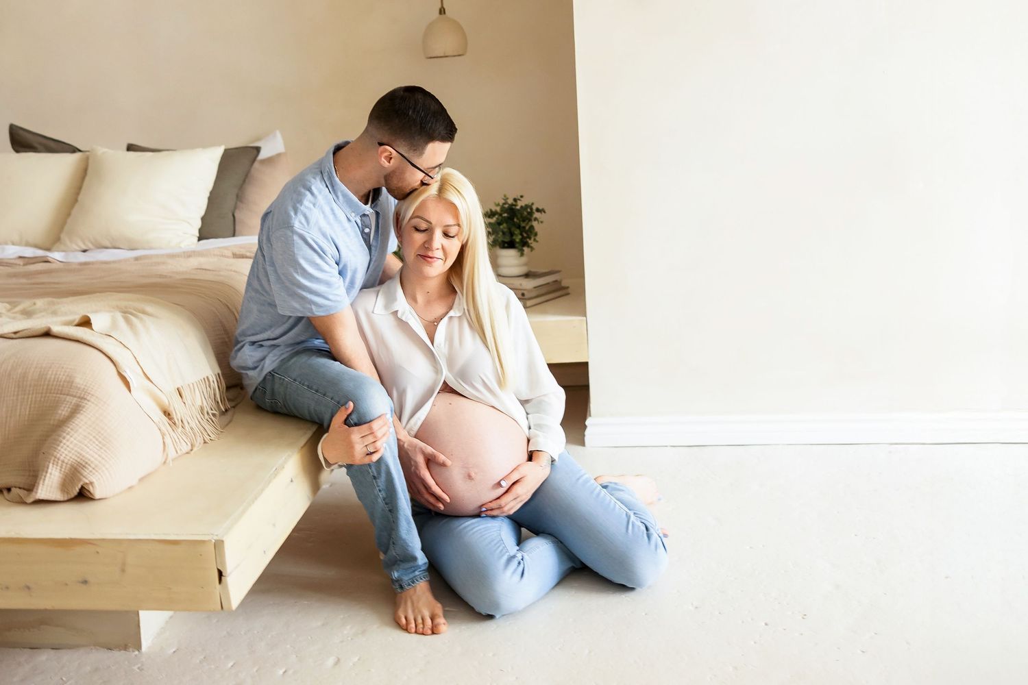 An intimate maternity photoshoot in a minimalist bedroom setting with neutral tones.