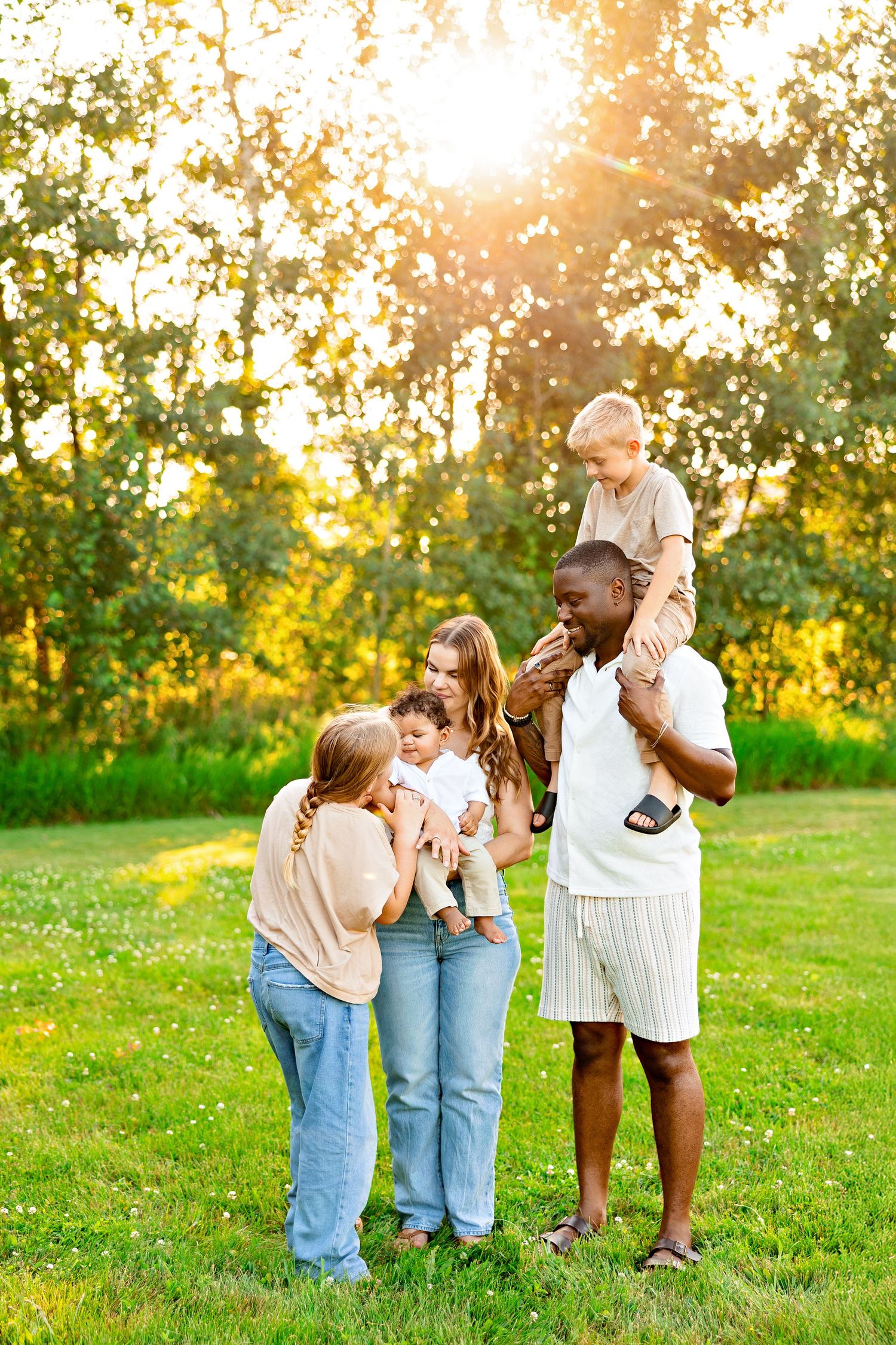 A mixed family enjoying quality time together on a sunny afternoon in a grassy field with golden sunlight filtering through trees.