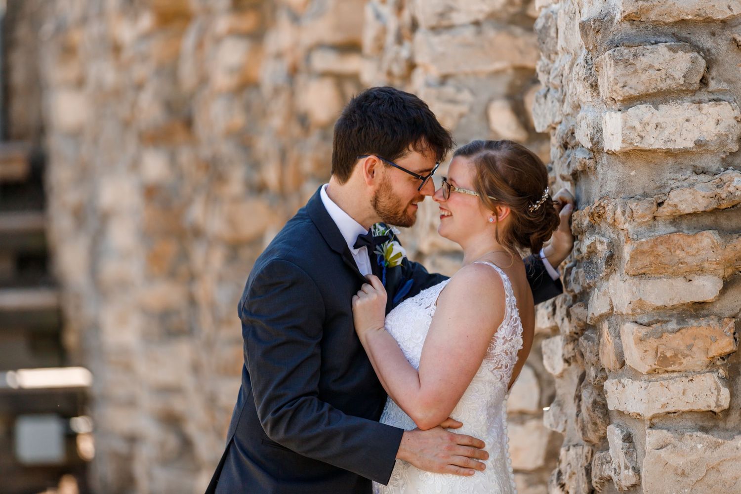 Intimate wedding portrait against rustic stone wall background during golden hour.