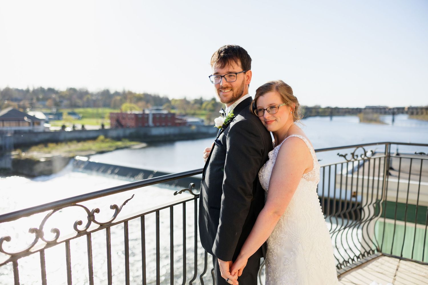 Couple poses together on balcony overlooking harbor with boats in background.