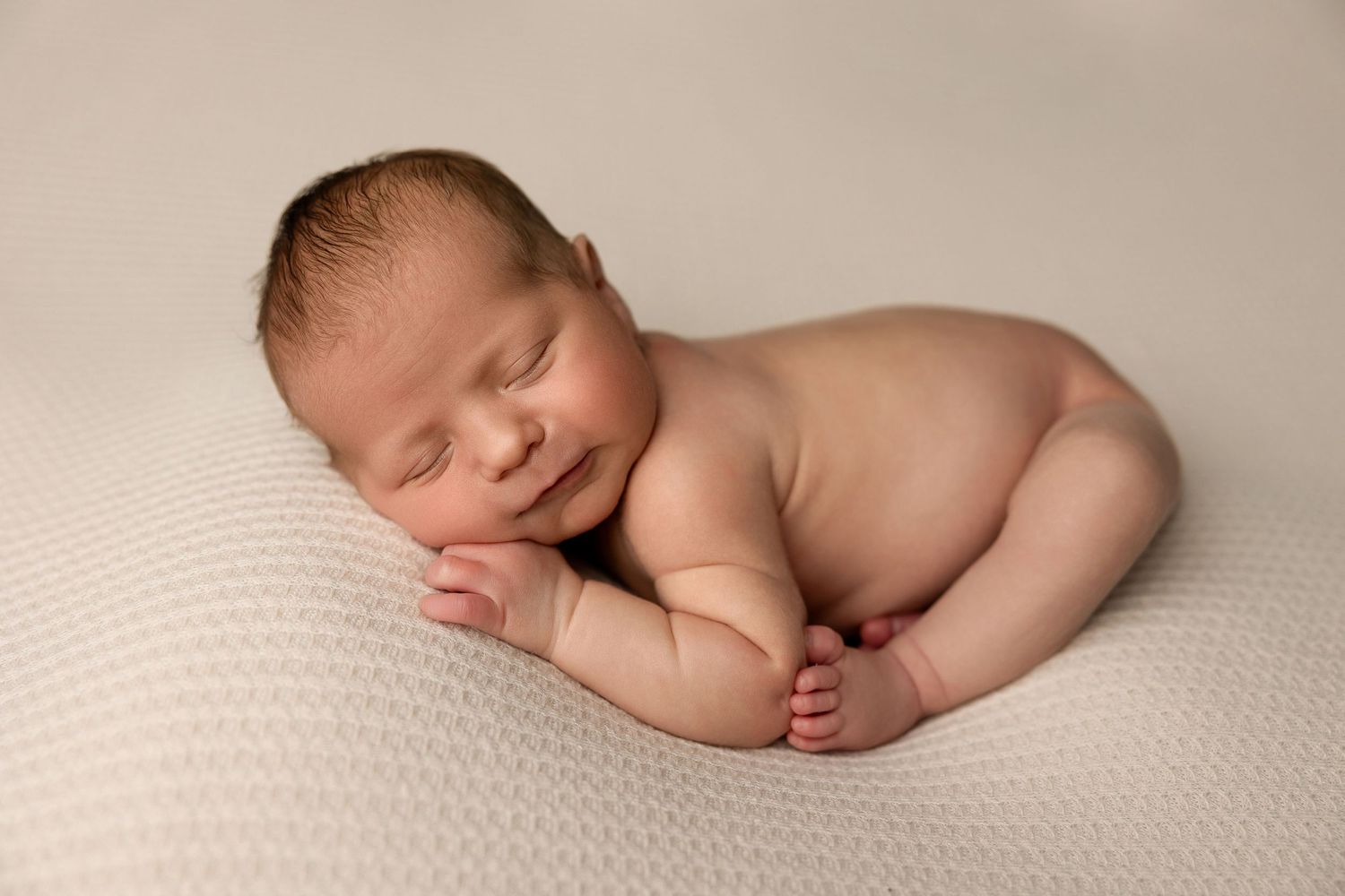 Peaceful newborn sleeping on cream textured backdrop during professional photo session.