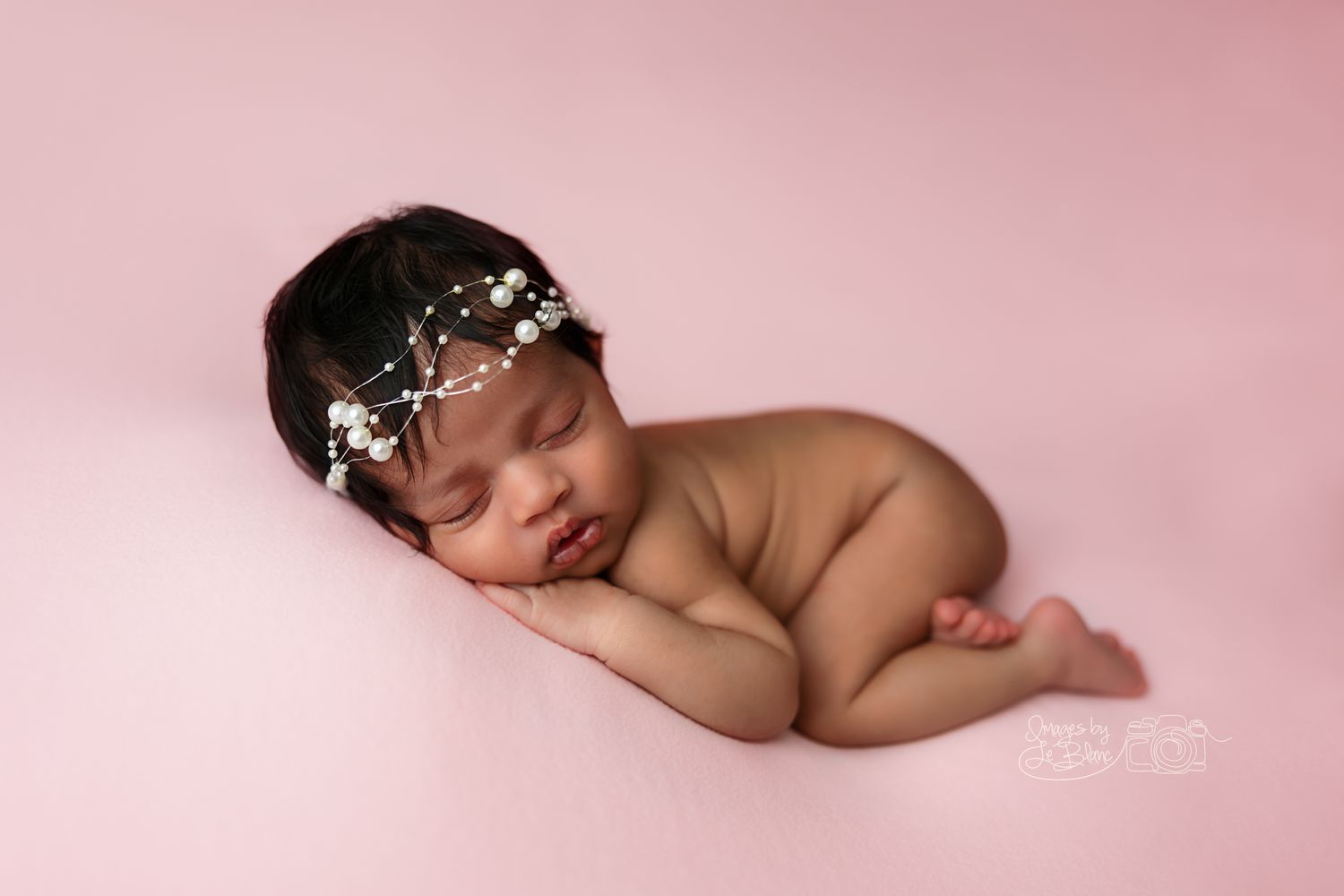 Sleeping newborn wearing delicate floral headpiece posed on pink backdrop.