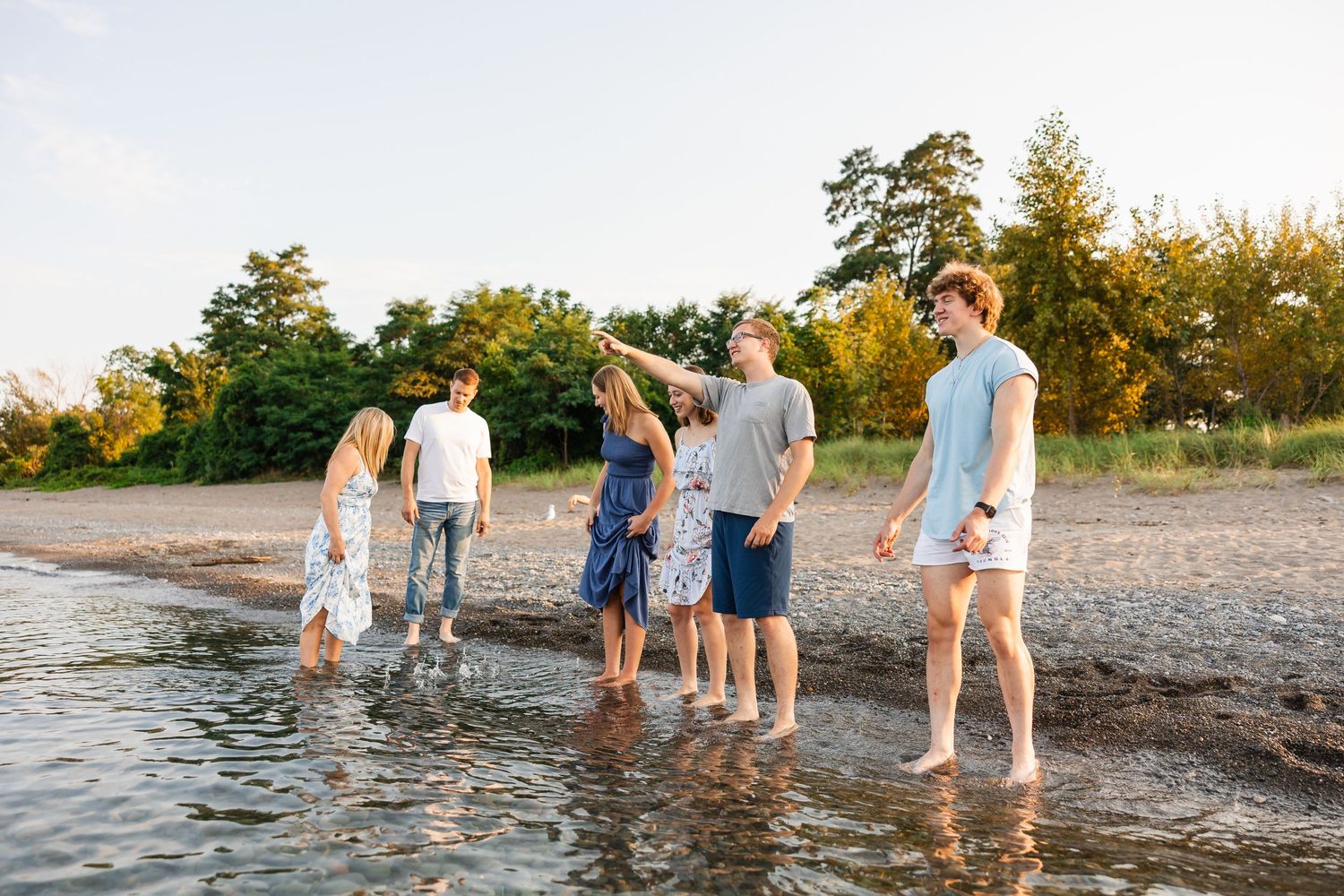 People walking together in shallow water along a peaceful beach shoreline during golden hour.