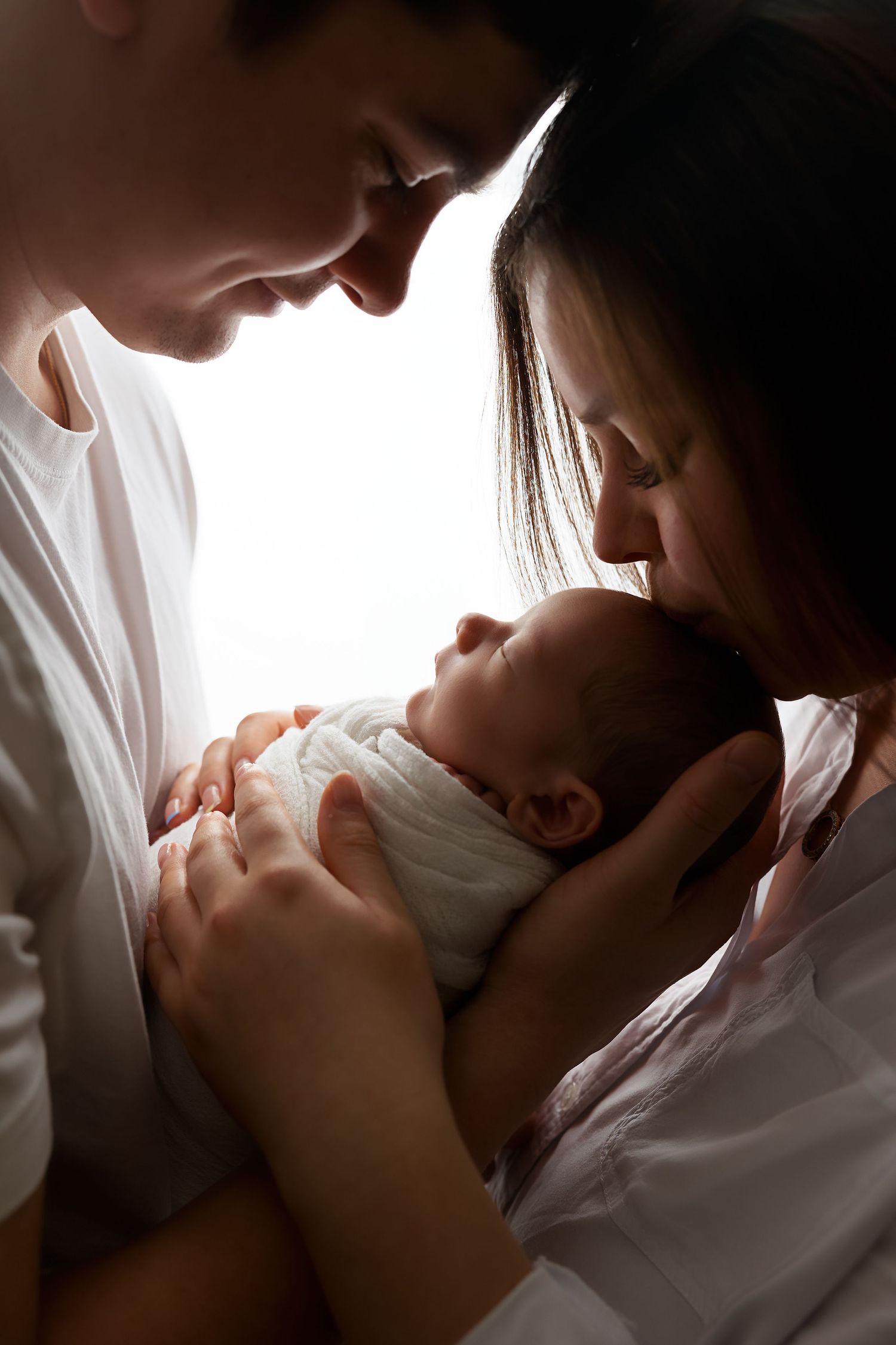 Parents sharing tender moment with newborn baby in dramatic lighting.