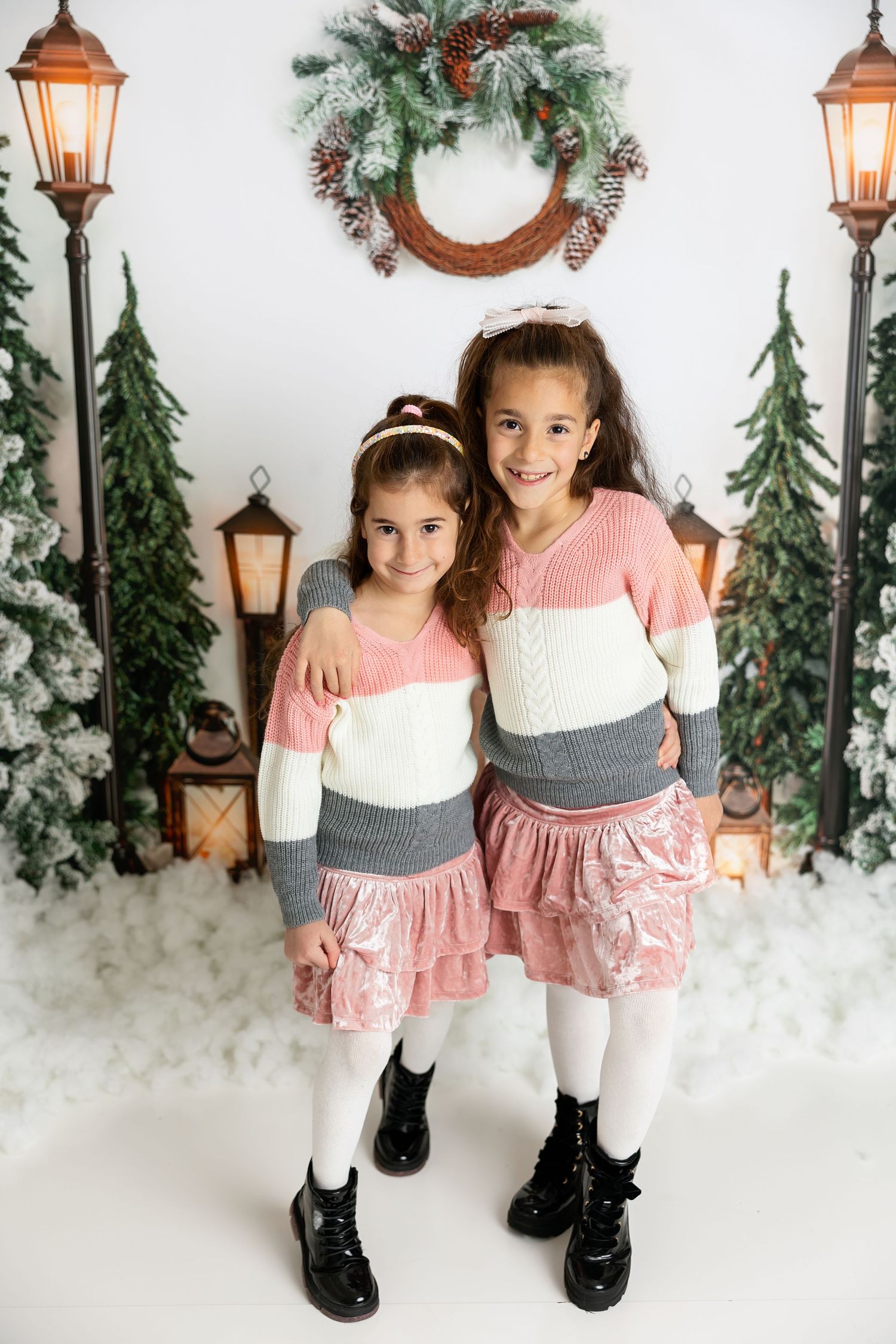 Two children in coordinating pink and grey outfits pose in front of Christmas backdrop.