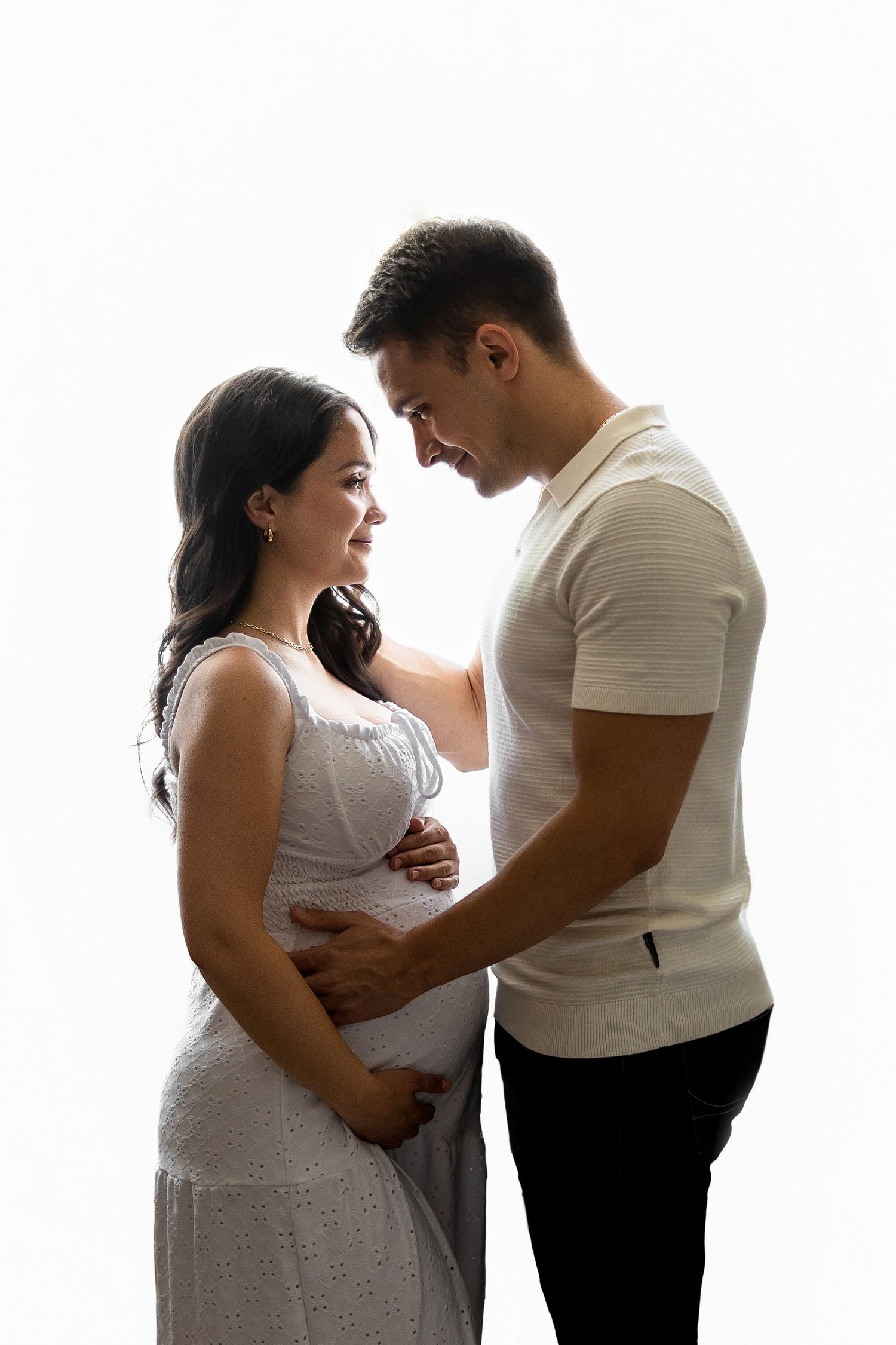 A pregnant woman and her partner share intimate moments in a maternity photoshoot series against a white background.