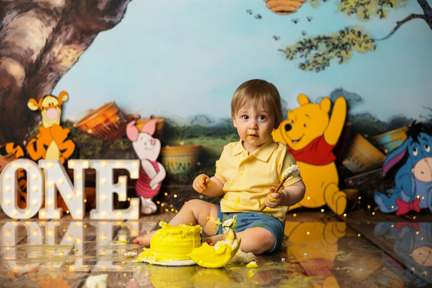 Baby's first birthday cake smash with Winnie the Pooh theme, featuring colorful character backdrop and ONE letter decorations.