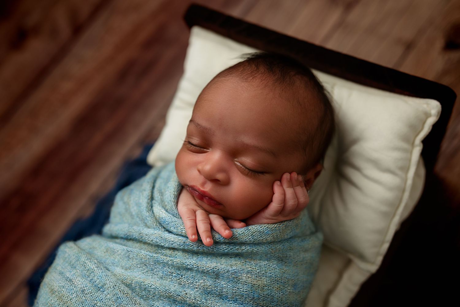 Sleeping baby wrapped in blue blanket resting head on white pillow.