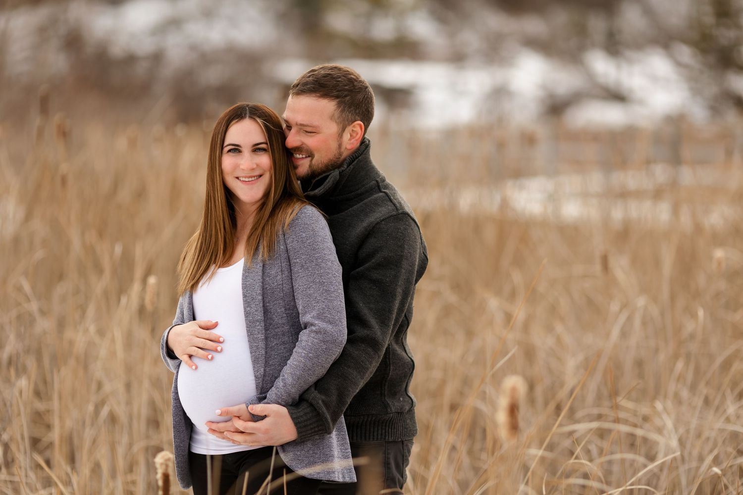 Couple sharing tender moment during winter maternity photoshoot in field.