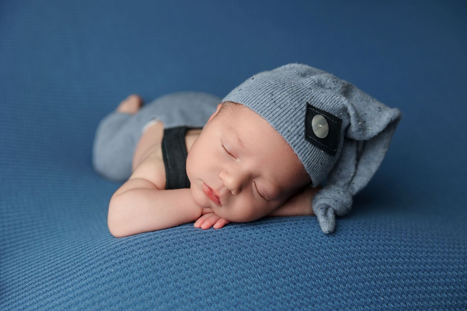 Peaceful sleeping newborn baby wearing gray swaddle blanket on soft blue textured background.
