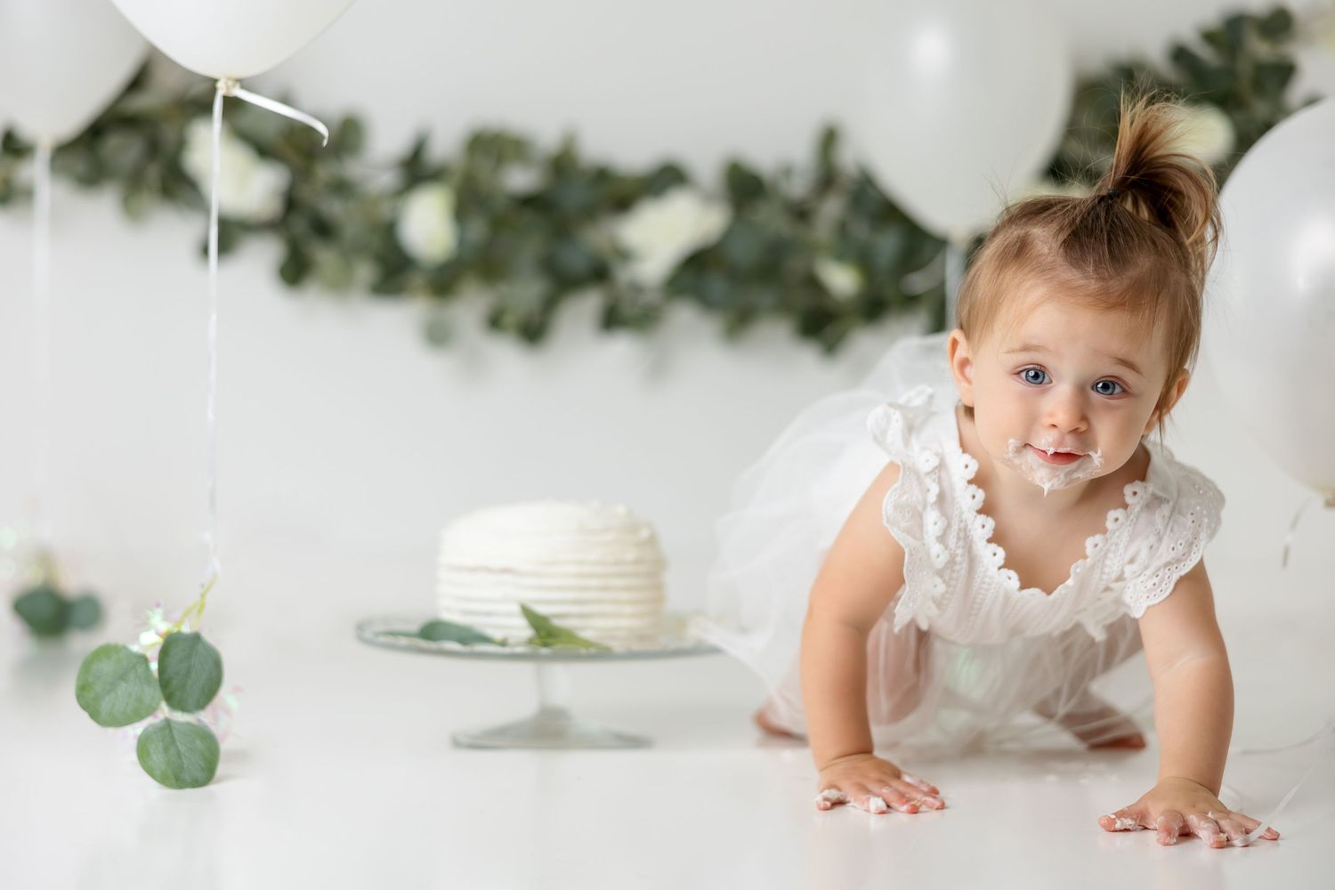 Elegant white and greenery first birthday photo session setup with eucalyptus accents.