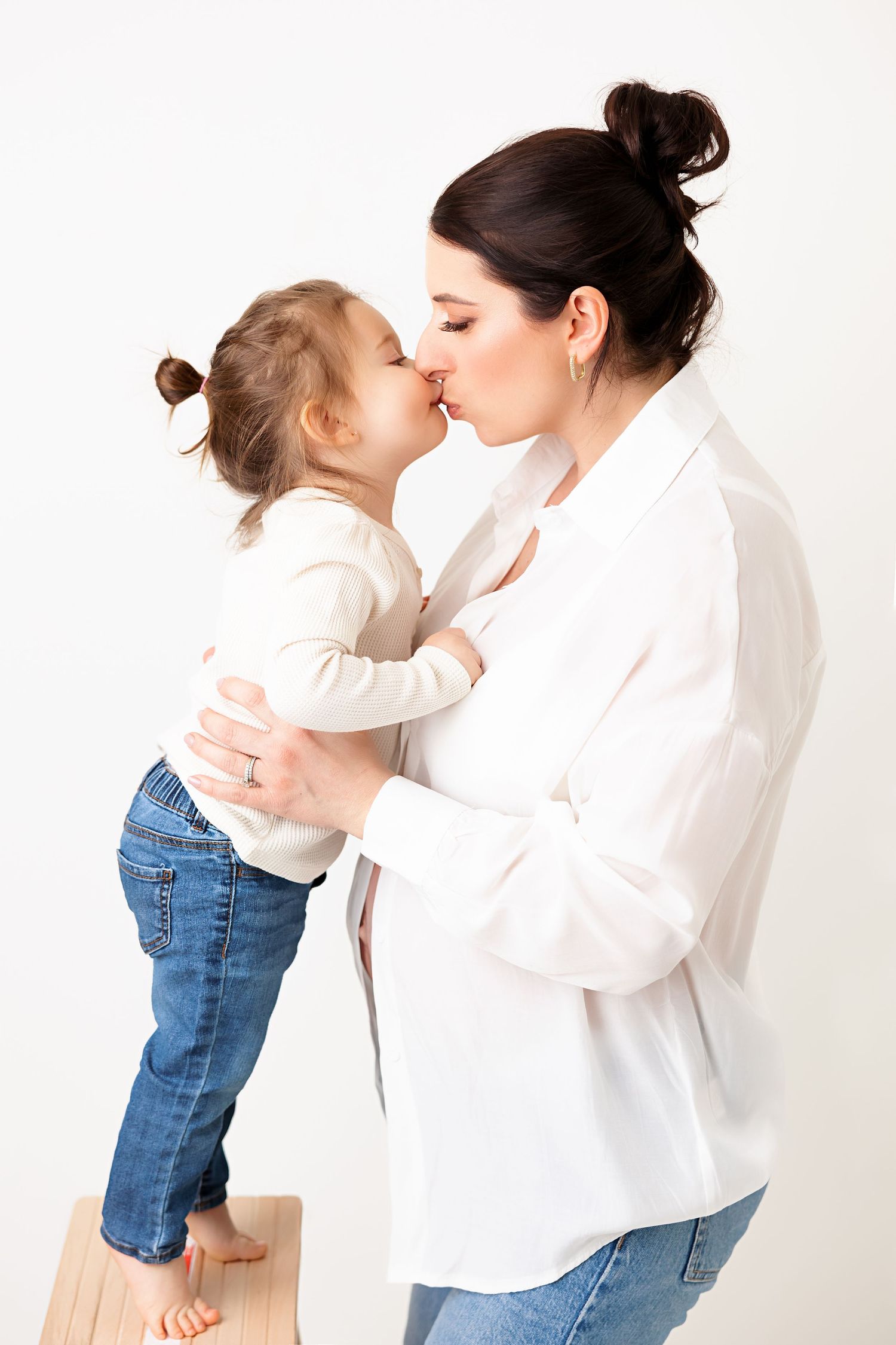 Sweet moment between child and mother in white shirt against minimalist background.