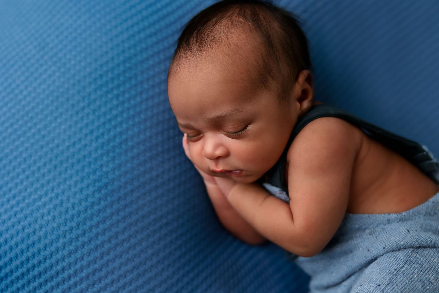 Sleeping newborn baby in blue wrap lying on textured blue background during peaceful slumber.