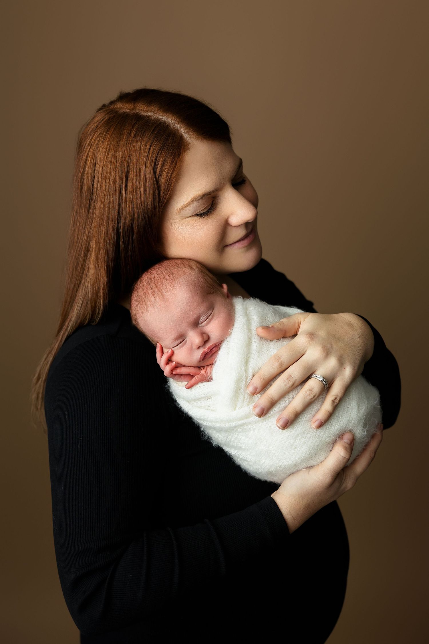 Tender moment between parent and sleeping newborn wrapped in white.
