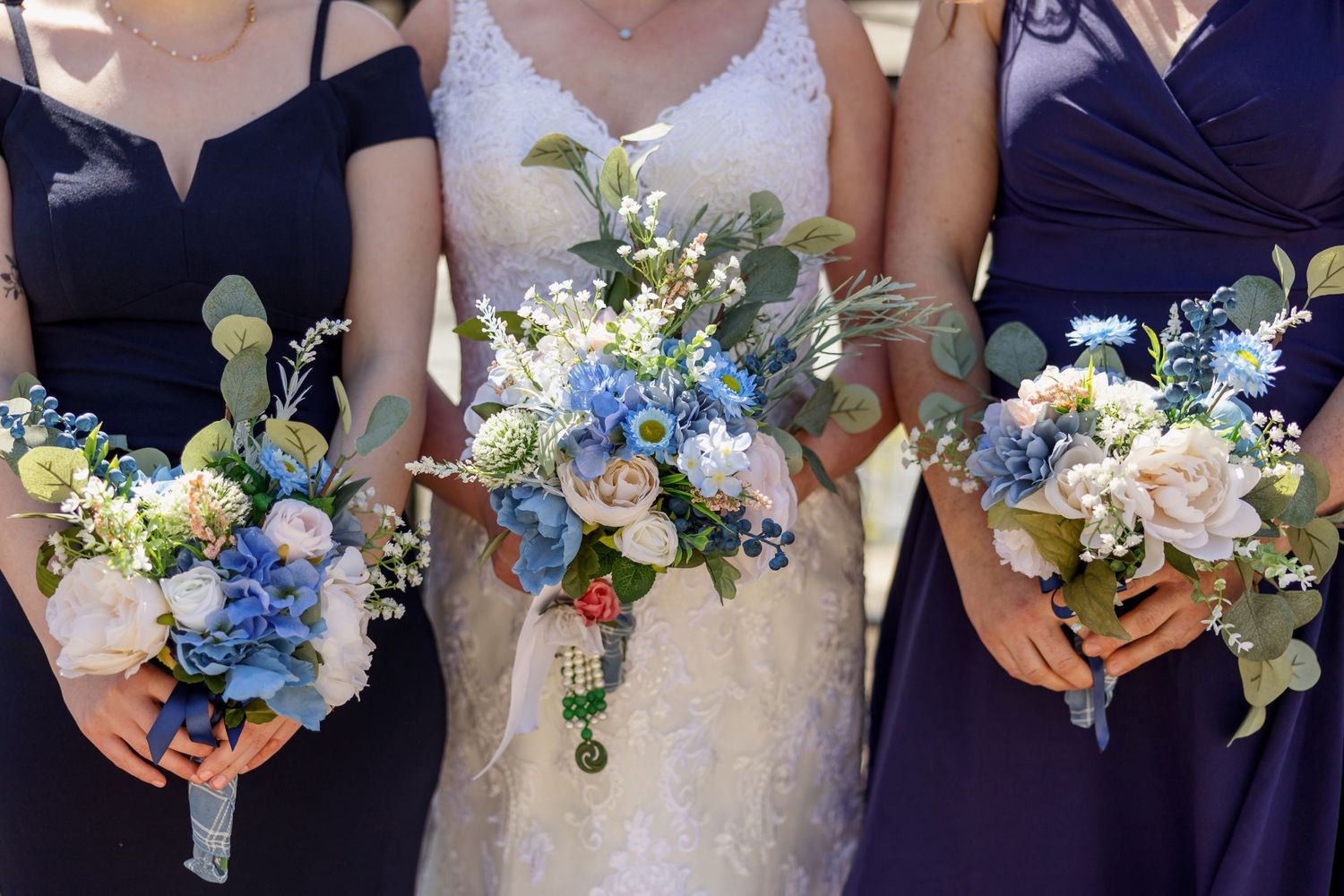 Three matching wedding bouquets in blue and white with greenery accents.
