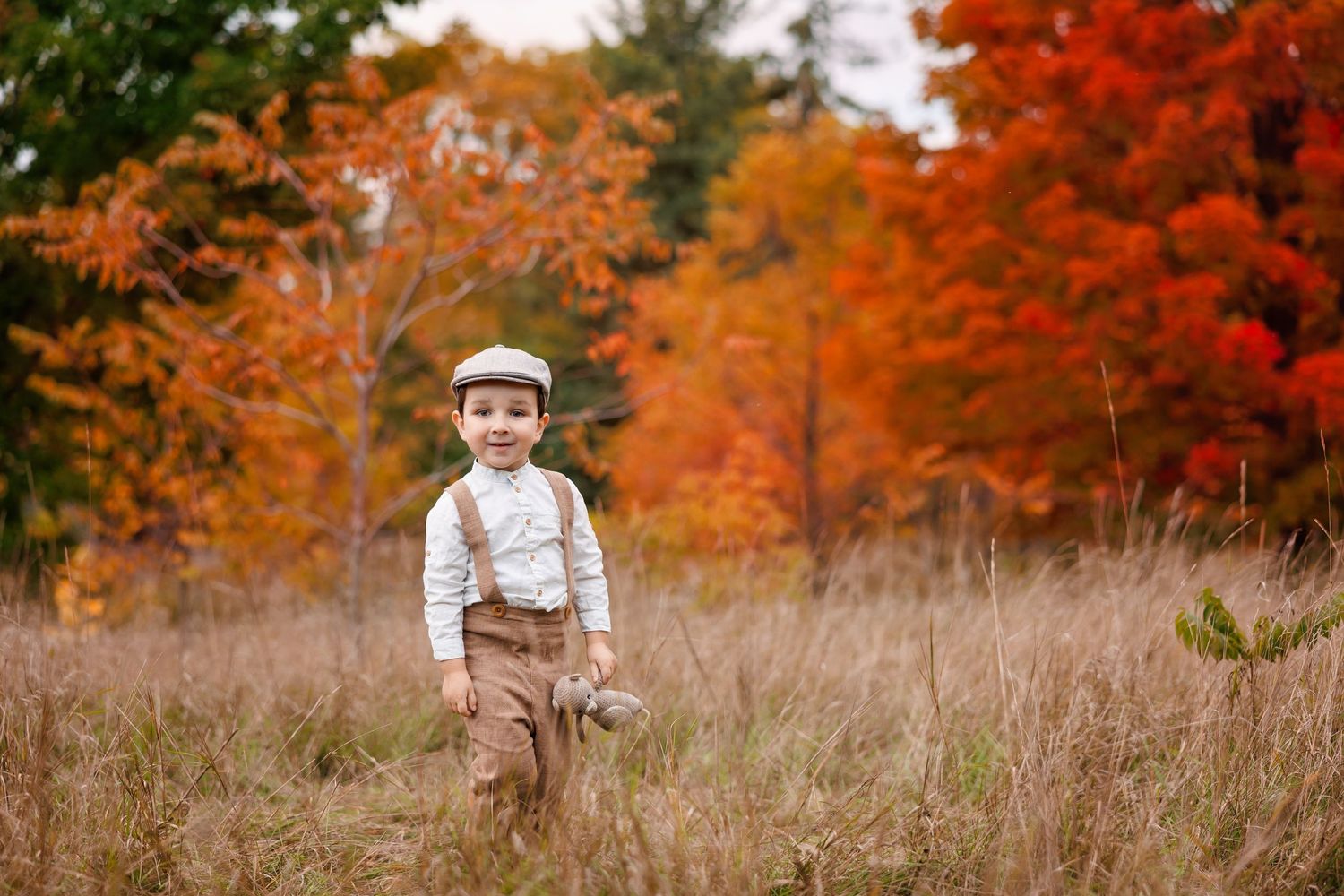 A small figure in vintage attire stands in a field with vibrant autumn foliage in the background.