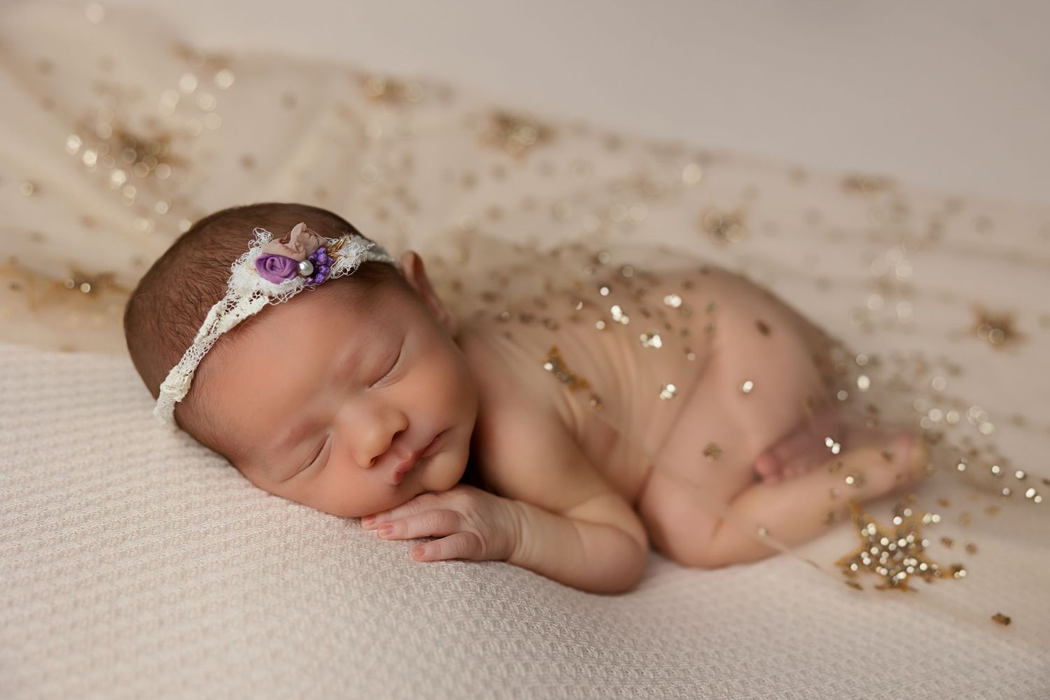 Sleeping newborn with sparkly details on cream backdrop.