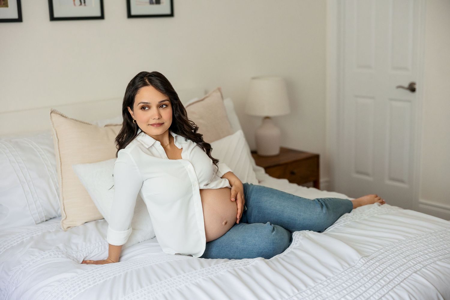 An intimate maternity photo session captured on a white bed with soft natural lighting.