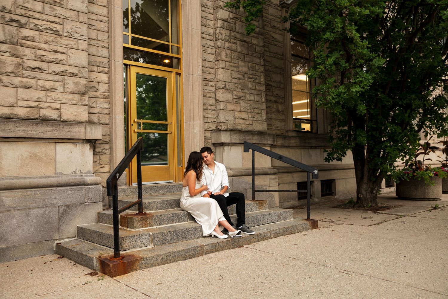 Couple sitting on stone steps outside a classic building, sharing an intimate moment during an engagement photo session.