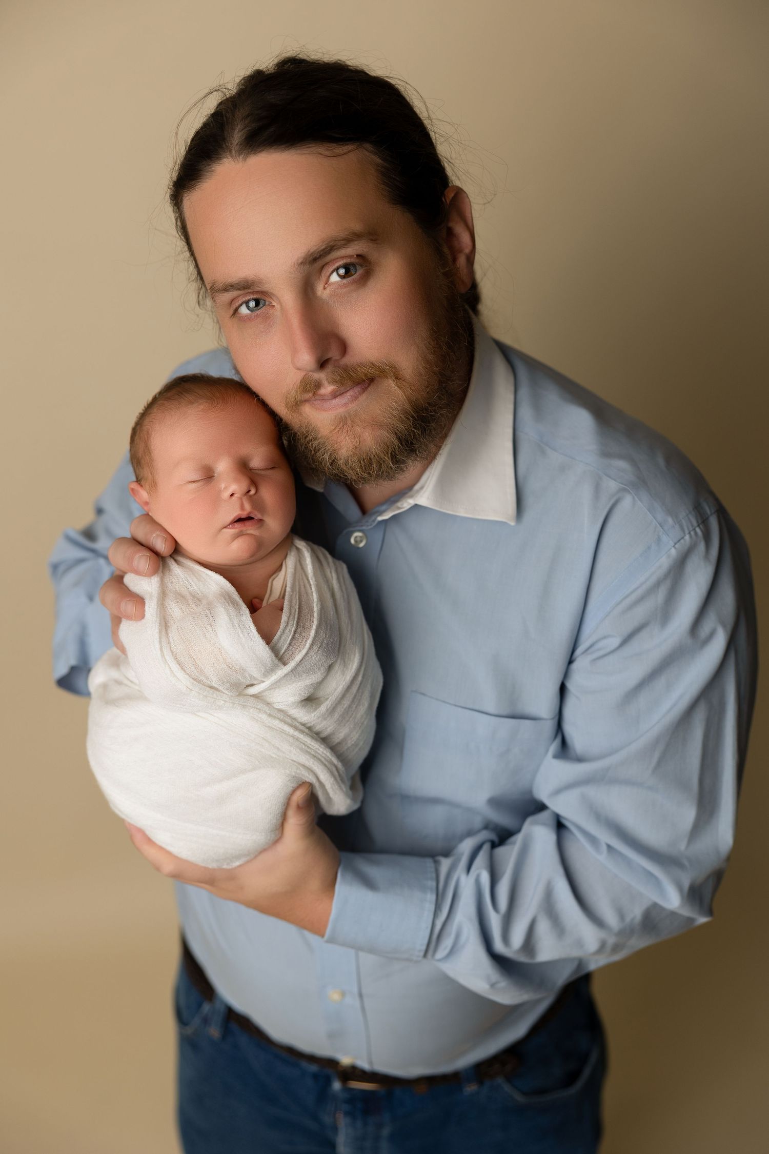 A tender portrait of someone holding a sleeping newborn baby while wearing a light blue button-down shirt.