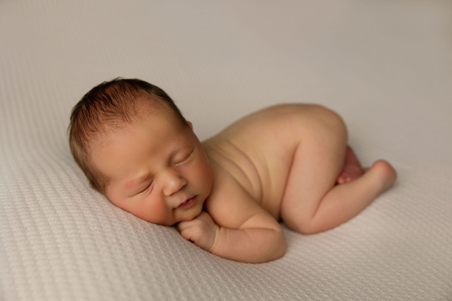 Peaceful sleeping newborn posed on neutral textured background.
