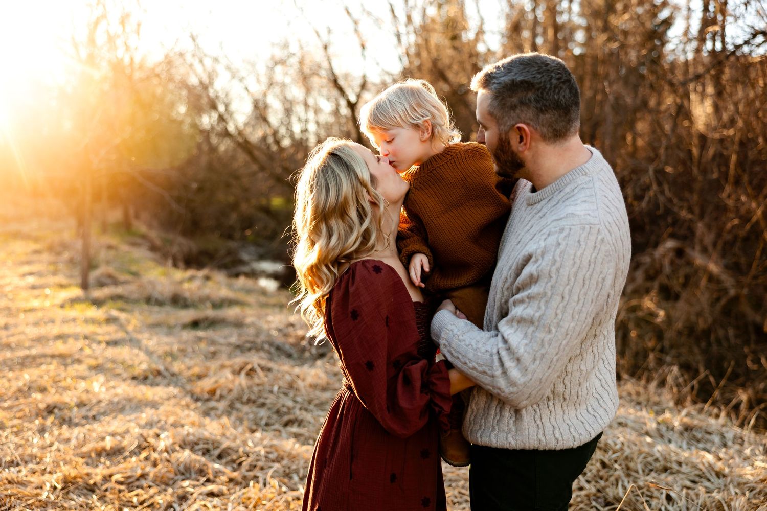 An intimate family portrait bathed in golden sunset light among autumn foliage.