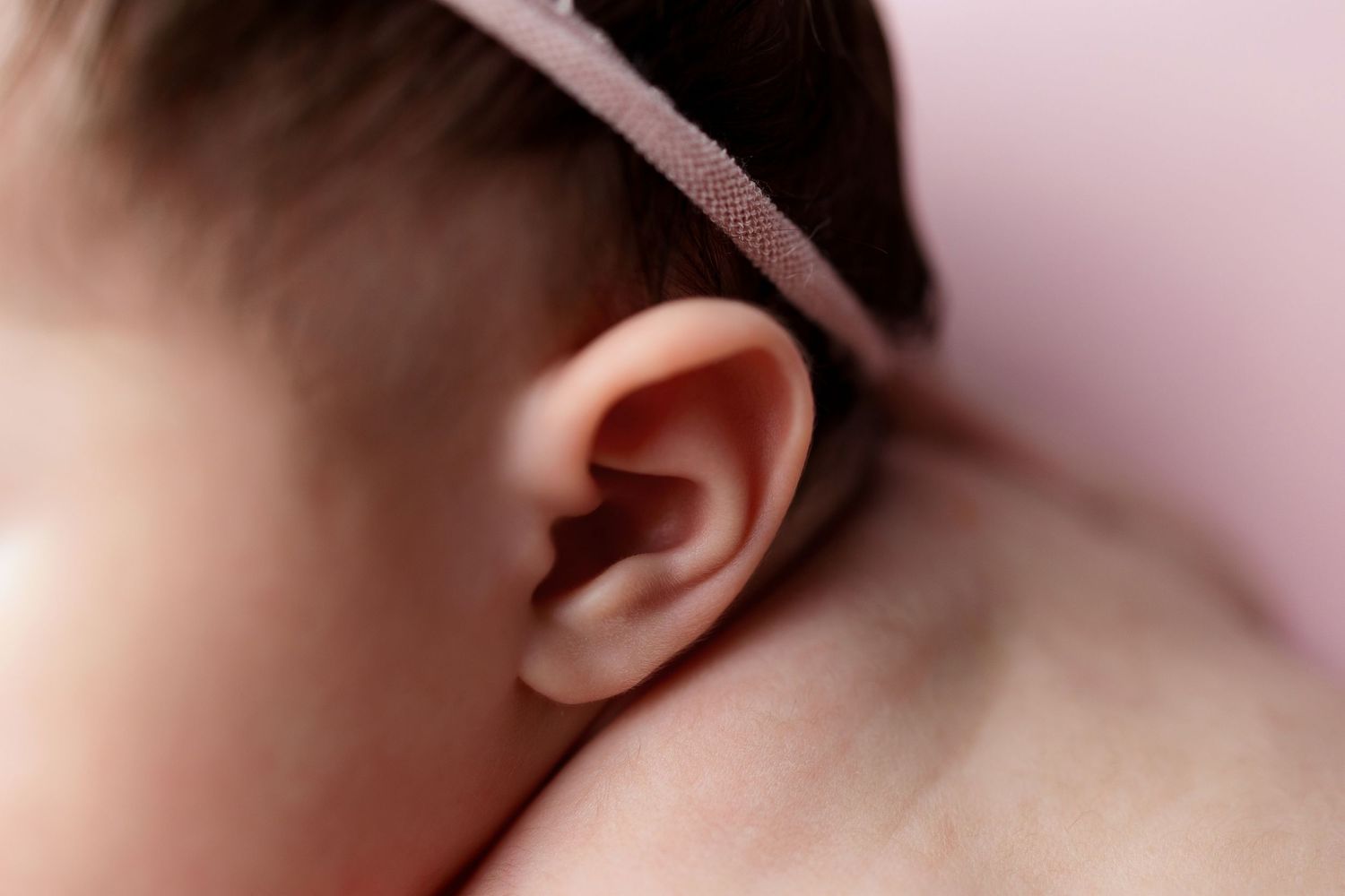Close-up detail of a baby's ear with soft pink lighting in the background.
