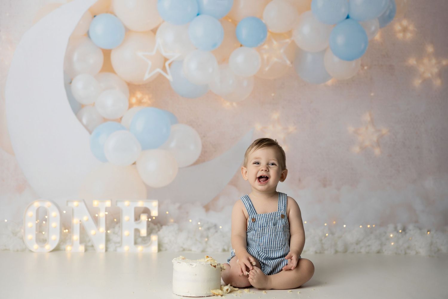 Balloon arch with blue and white decorations creates a festive backdrop for a baby's first birthday celebration scene.