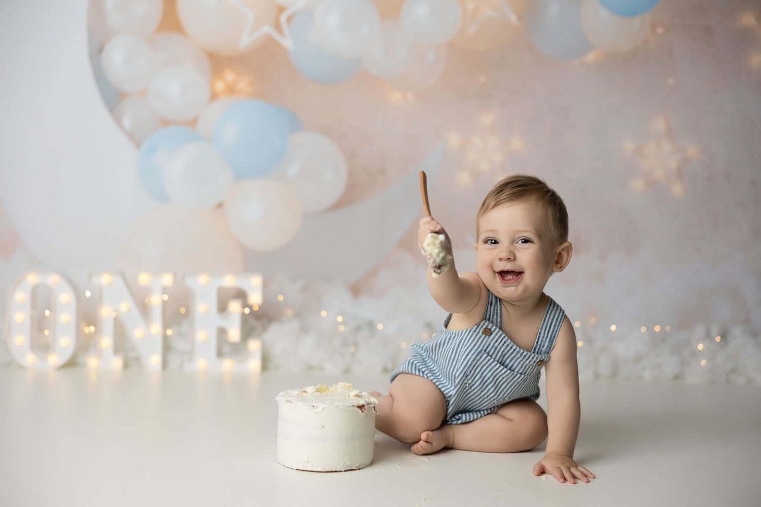 Collage of four photos with balloons and twinkling lights showing a one year birthday cake smash celebration.
