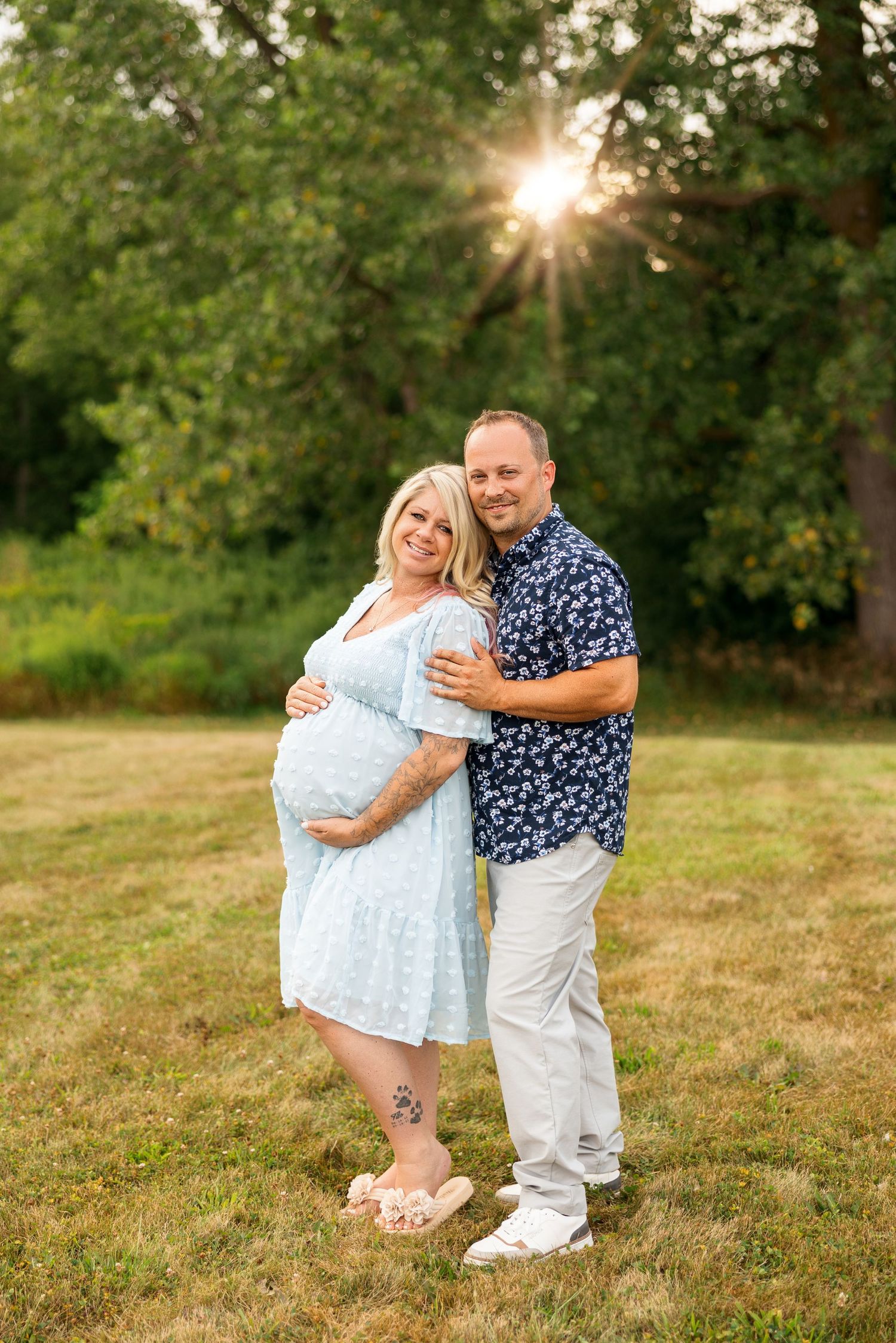 A couple embraces joyfully in a grassy field during golden hour sunset, creating a romantic outdoor portrait series.