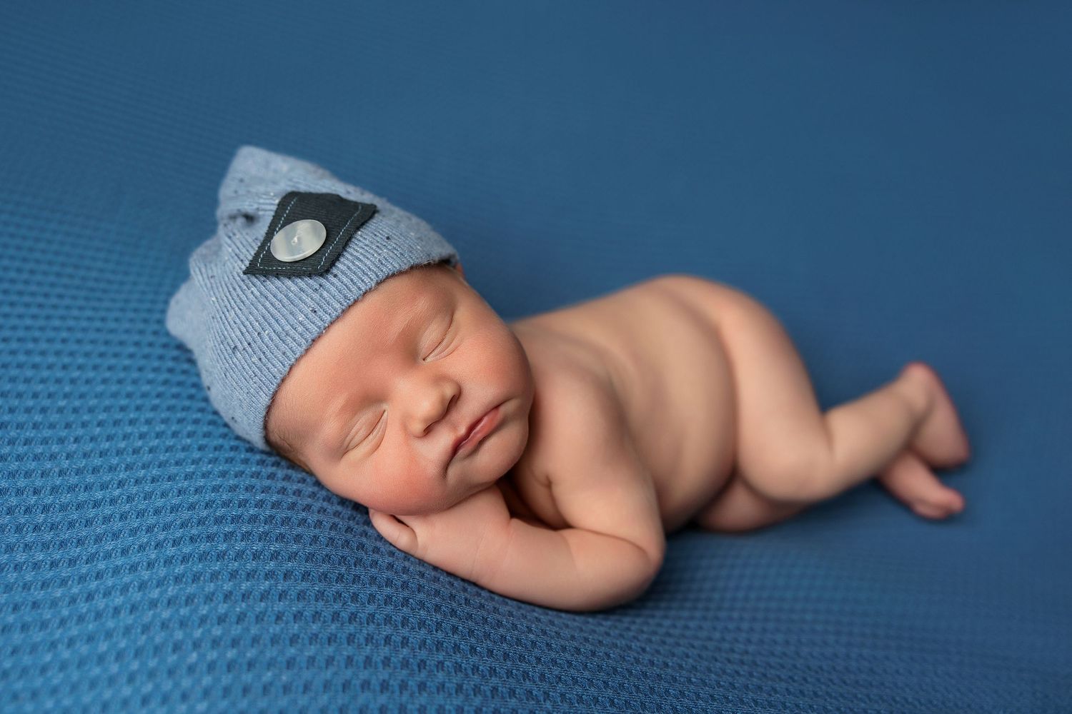 Sleeping newborn baby lying on soft blue textured backdrop in professional studio setting.