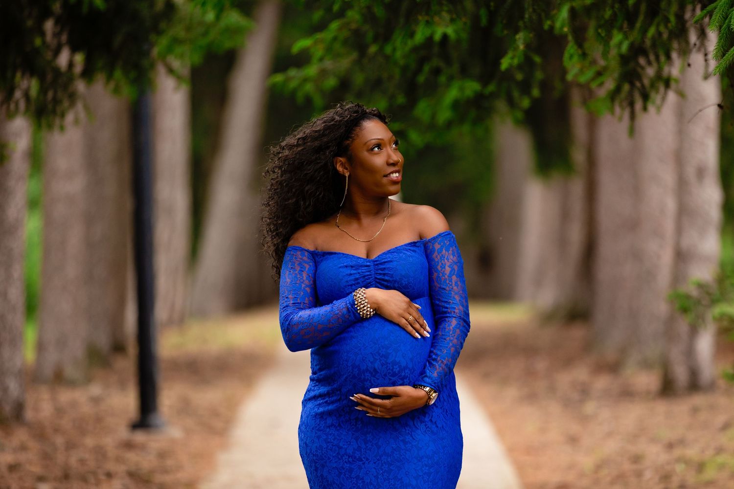Romantic maternity session with couple in blue dress and formal wear among trees.