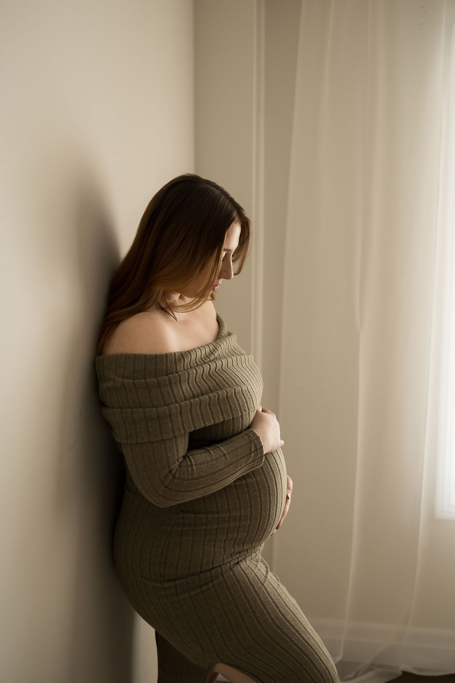 A person in a cozy gray sweater poses near a window in soft natural light.