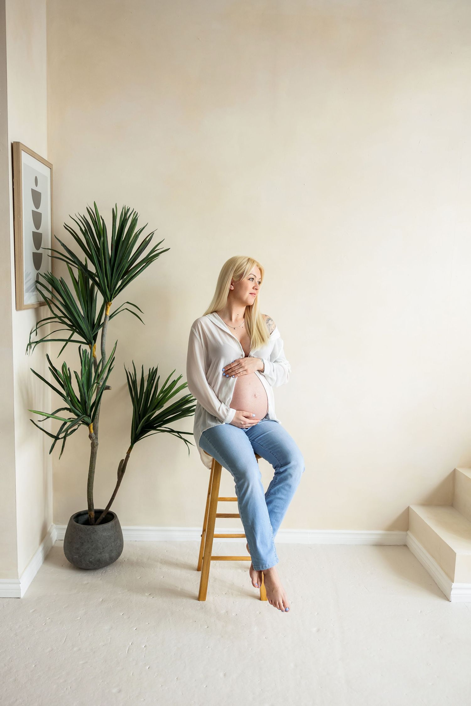 Artistic maternity portraits in a bright interior space with modern decor and palm plants.