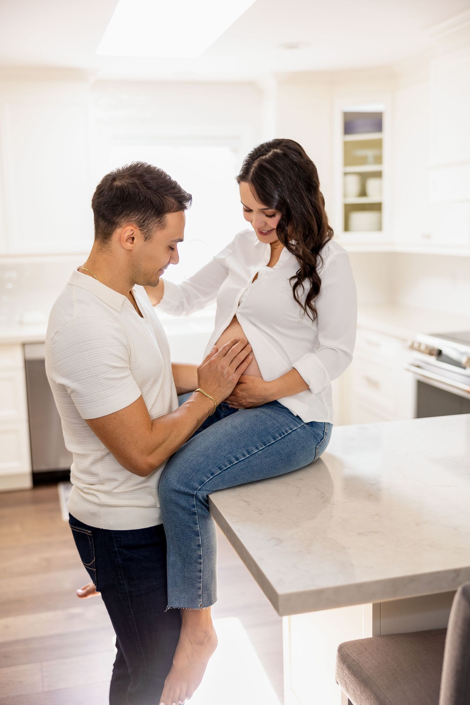 Intimate maternity photos captured in a modern white kitchen with natural lighting.
