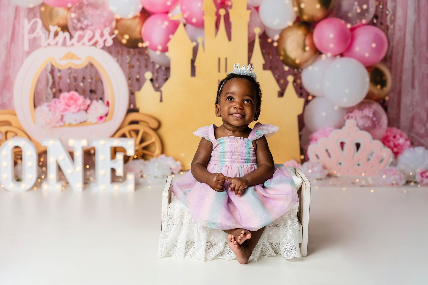 First birthday celebration photo with pink balloon arch and castle backdrop.