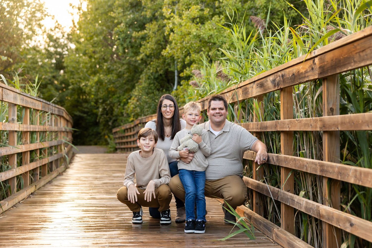 A family poses together on a wooden boardwalk surrounded by lush greenery on a sunny afternoon.