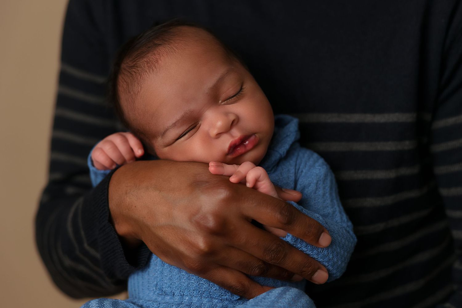 Sleeping baby in blue outfit rests peacefully in caring hands.
