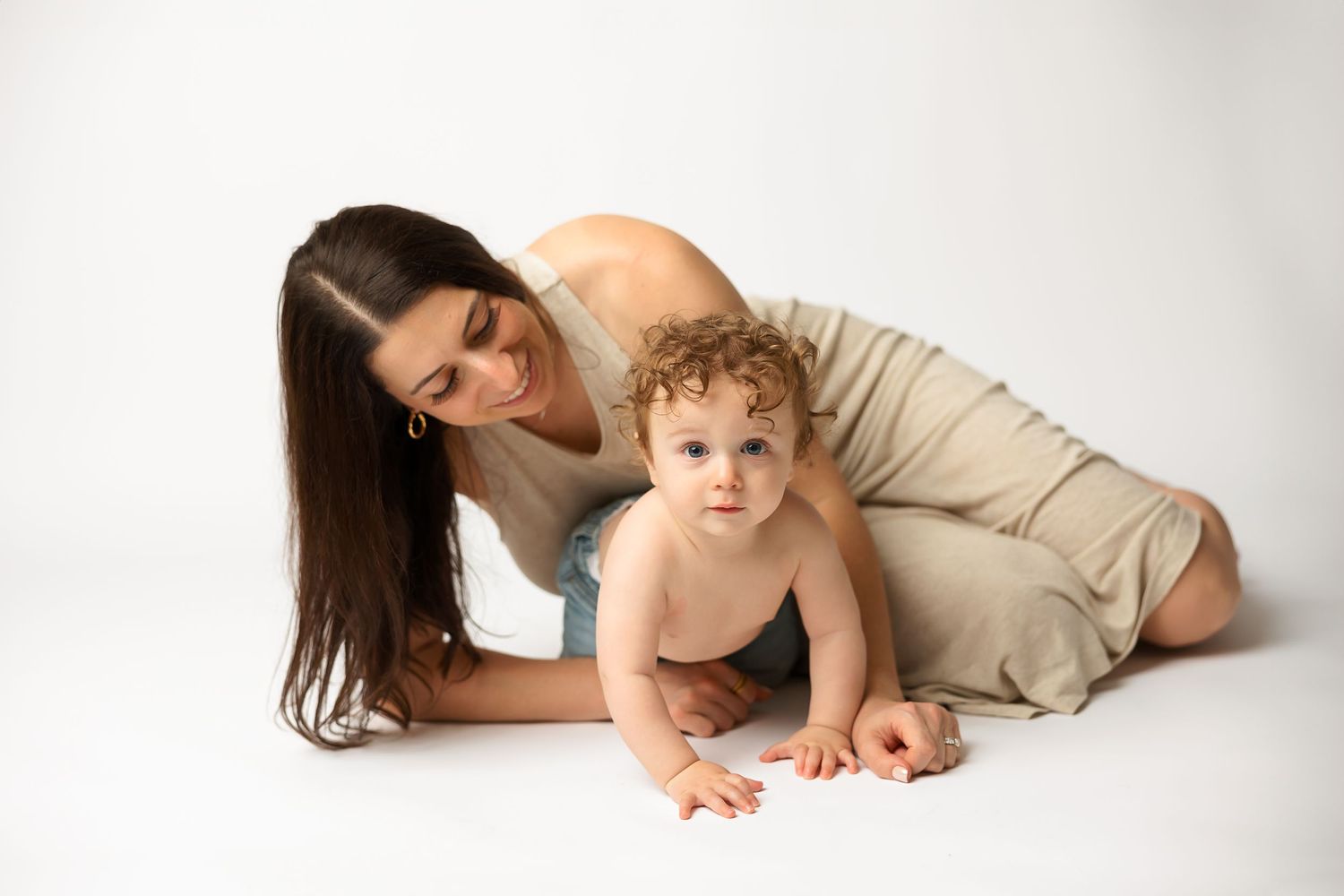 Mother and baby in natural tones lying together on white studio background.