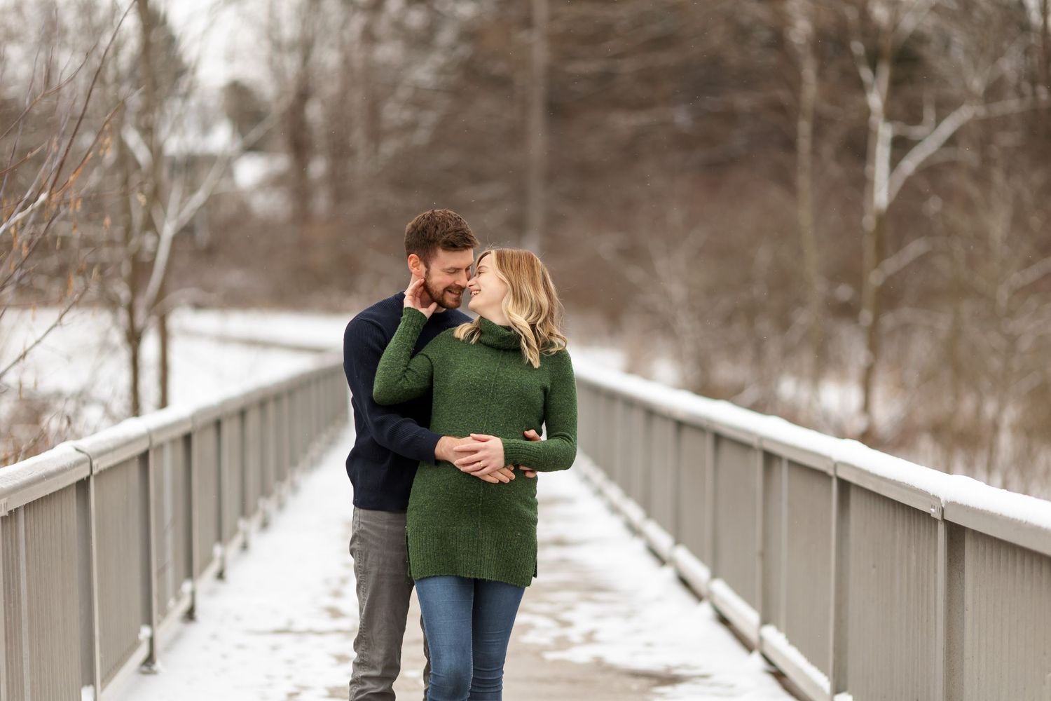 Couple sharing intimate moment on snow-covered bridge in winter setting.