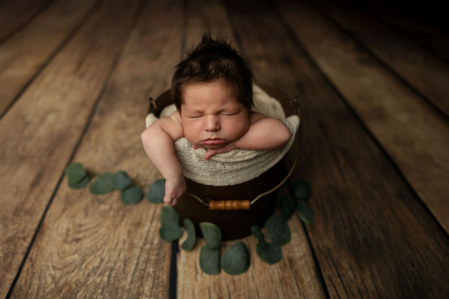 Sleeping newborn baby rests peacefully on rustic wooden backdrop with green leaf accents.