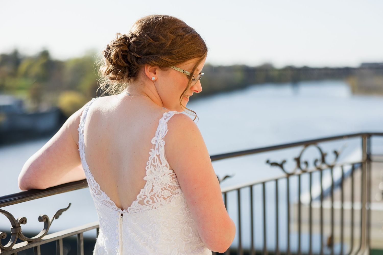 Beautiful lace wedding dress with open back detail shown against waterfront railing and river view.