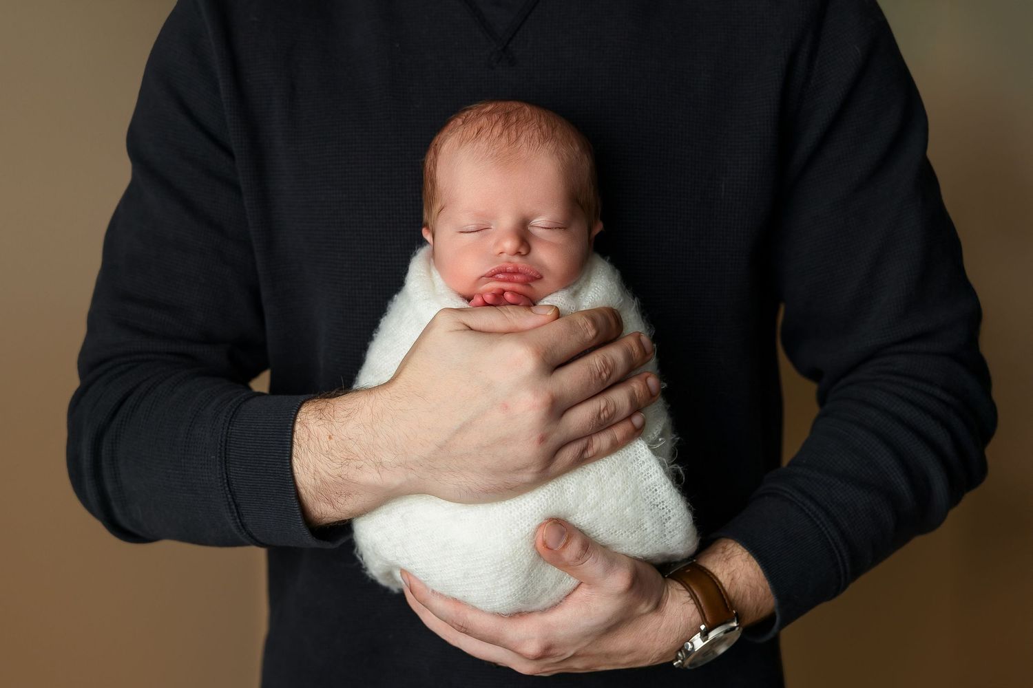 Close-up of swaddled newborn held against dark sweater.